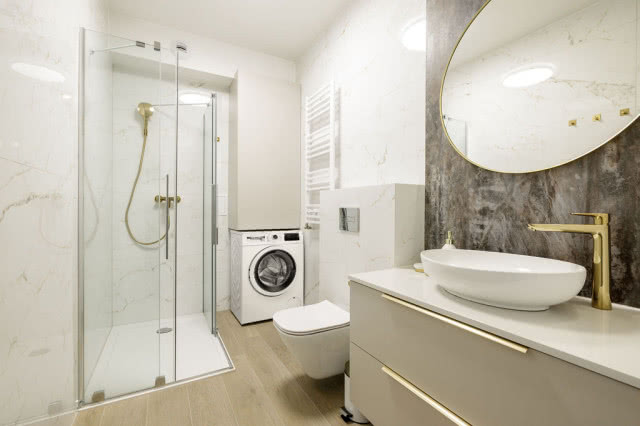 łazienka, kabina prysznicowa, pralka, owalne lustro w złotej ramie, grzejnik, sedes, umywalka nablatowa