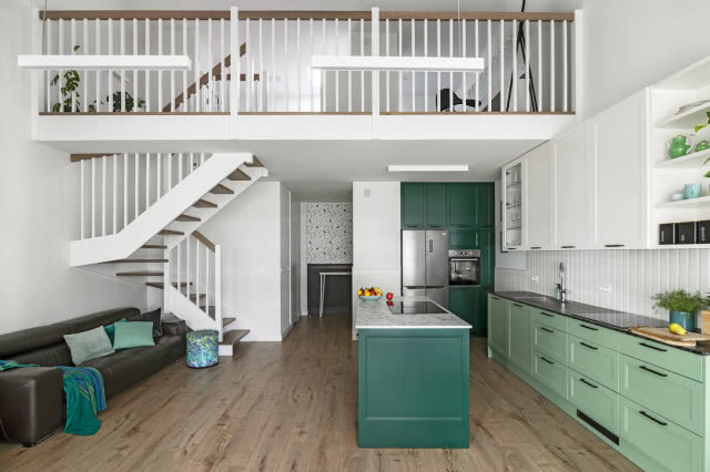 wyspa kuchenna, zielone fronty kuchenne, półki, białe płytki na ścianie, płyta grzewcza, kwiaty, lodówka, piekarnik, schody, antresola, kanapa, koc, pufa