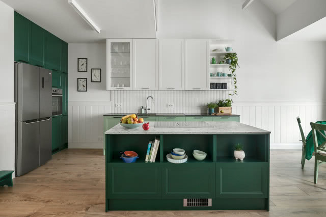 wyspa kuchenna, zielone fronty kuchenne, półki, białe płytki na ścianie, płyta grzewcza, obrazki, kwiaty, lodówka, piekarnik, krzesła