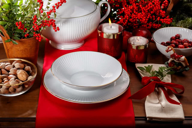 drewniany stół, czerwony bieżnik, biała porcelana, ze złotą otoczką, świecznik, orzechy, waza, kwiat w wazonach