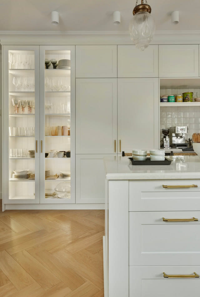 Stylowa biała kuchnia z podświetloną witryną i złotymi uchwytami szafek