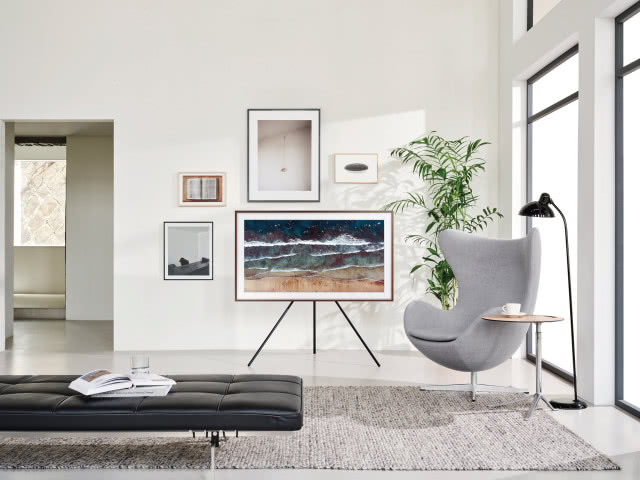 Szezlong, szary dywan, telewizor na stojaku, obrazy na ścianie, szary fotel, czarna lampa stojąca