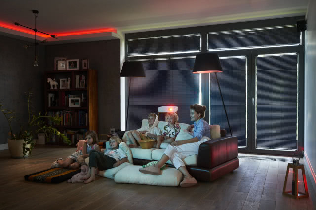 Granatowe żaluzje Anwis, czarne lampki sufitowe, czarna kanapa.