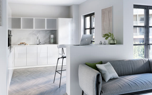 białe meble kuchenne, stołki barowe, ścianka z blatem , szara kanapa, laptop, wazon z trawą, jodełka na podłodze