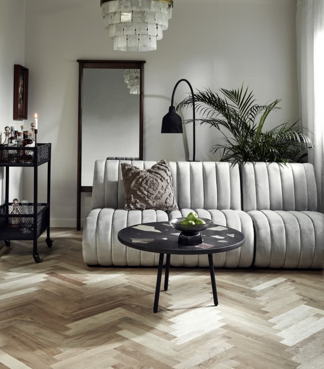 Zdjęcie szarej, pikowanej sofy w salonie w stonowanych barwach