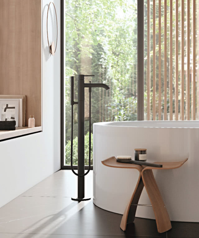 Bateria wannowo-natryskowa 
KLUDI BOZZ, drewniany stołek, szczotka do mycia, słoiczek, biała wanna wolnostojąca, okno
