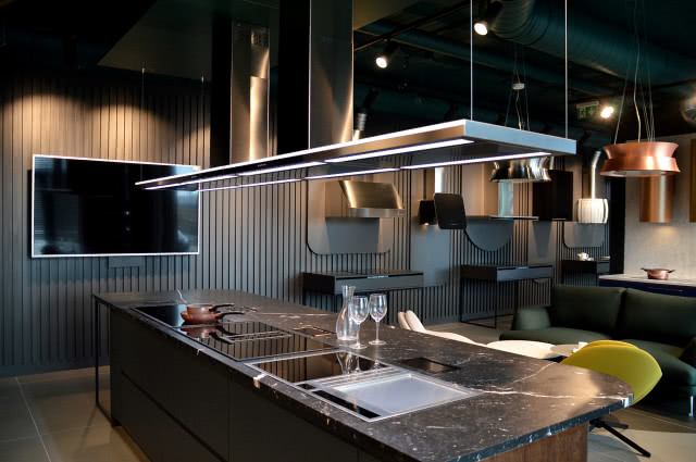 dwie lampy wiszące nad stolikiem kawowym, żółty fotel, pudrowy róż fotel, kuchnia, wyspa kuchenna, okap nad wyspą kuchenną, żaluzje, kanapa, telewizor, kieliszki