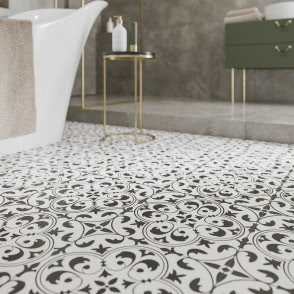 kolekcję Naomi, wanna wolnostojąca biała, na podłodze płytki czarno-białe, na ścianie płytki imitujące beton, owalne lustro ze złotą ramą, prysznic ze złotymi bateriami i deszczownicą, szafka na złotych nóżkach w odcieniu zieleni