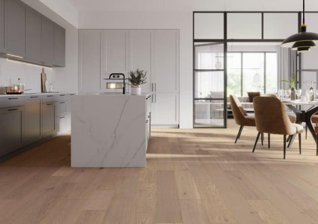 drewniana podłoga, wyspa kuchenna, czarna bateria zlewozmywakowa, okrągły stół z krzesłami, białe meble kuchenne, kieliszki, szampan, wino