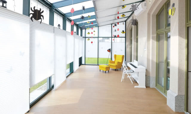 żaluzje plisowane, żółty fotel i podnóżek, fortepian, krzesło lampa podłogowa, ozdoby wiszące,