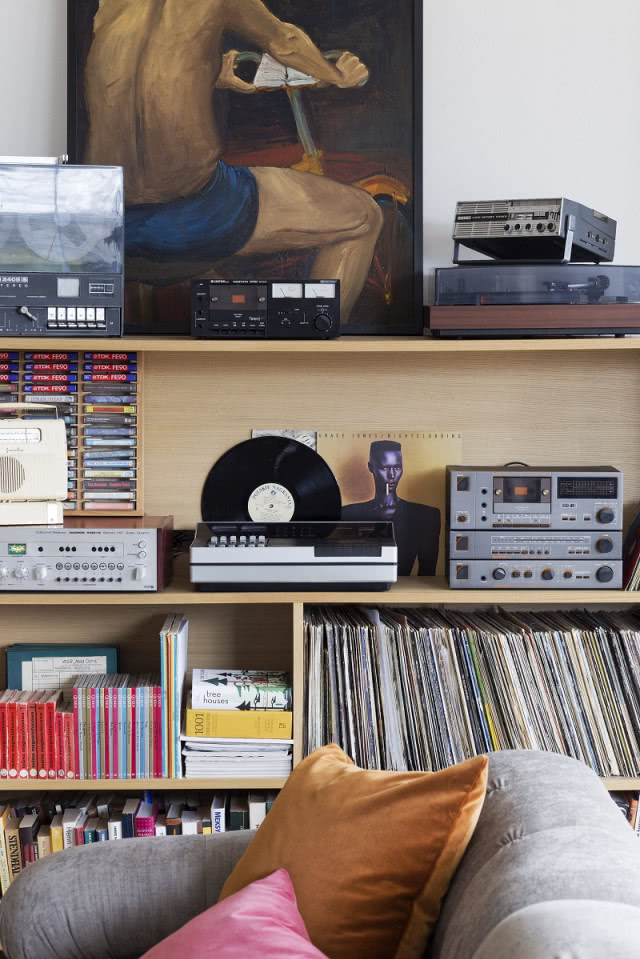 Kolorowe poduszki na sofie, półki na książki, płyty, sprzęt grający.