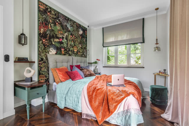 Tapeta marki Moooi kupiona w Walldecor wprowadza do sypialni egzotykę, do której klimatu świetnie pasują mocne kolory tkanin. Stoliki nocne, złota konsola i aksamitny puf stanowią elegancką i spokojną przeciwwagę, dzięki czemu sypialnia jest eklektyczna, ale i szykowna.