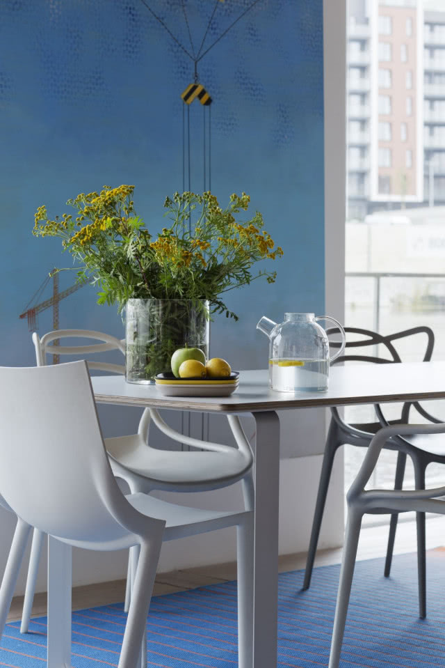 Świeże kwiaty i niebieskie ściany we wnętrzu, biały stół z białymi krzesłami, dzbanek , owoce oraz wazon z kwiatami