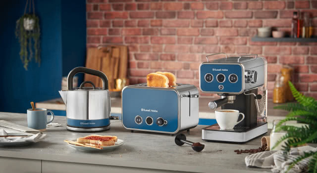 elektryczny czajnik, toster, ekspres do kawy, wyspa kuchenna, cegła na ścianie, filiżanka z kawą, tosty z dżemem, paprotka, półki, kubek