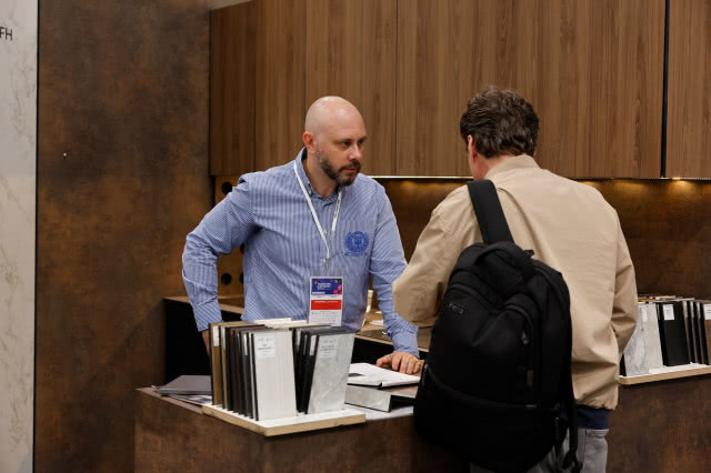 Rozmowa przedstawiciela firmy z odwiedzającym przy stoisku z próbkami materiałów wykończeniowych podczas targów branży wnętrzarskiej