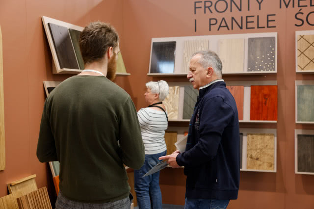 Uczestnicy targów oglądają i omawiają próbki frontów meblowych oraz paneli dekoracyjnych na stoisku wystawowym