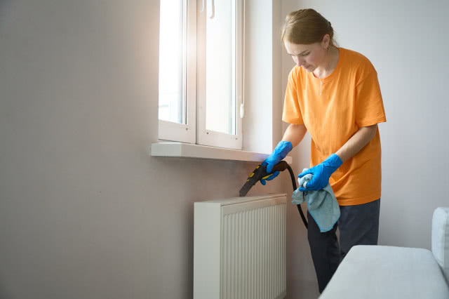 kobieta czyści grzejnik odkurzaczem 