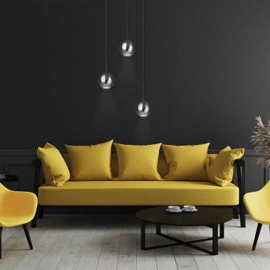Lampy wiszące Bola Bola LED, żółta kanapa, żółte fotele na czarnych nogach, ciemno szare ściany, drewniana podłoga, filiżanki, czarny okrągły stolik kawowy