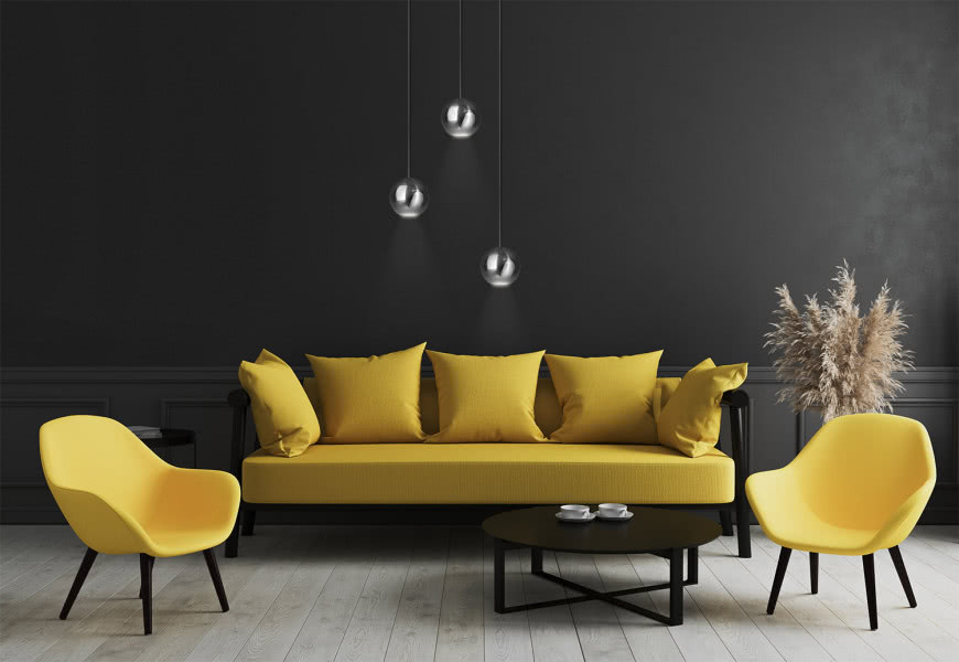 Lampy wiszące Bola Bola LED, żółta kanapa, żółte fotele na czarnych nogach, ciemno szare ściany, drewniana podłoga, filiżanki, czarny okrągły stolik kawowy