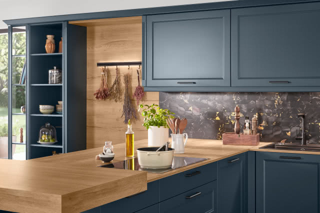granatowe meble kuchenne, crewniane blaty, półwysep kuchenny, regały, okap, piekarnik, duży drewniany stół z krzesłami, belki stropowe