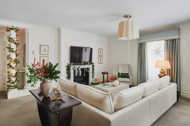 biały narożnik, stolik kawowy, oświetlenie sufitowe, lampy biurkowe, zasony, firany, gwiazdy na oknie, drewniana witryna na bibeloty, obrazy, choinki, poduszki ozdobne, koc, fotel