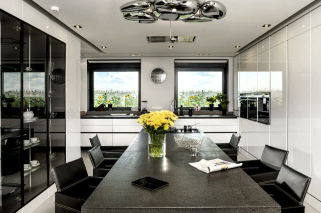 Model 019, zestaw mebli kuchennych z frontami wykończonymi białym błyszczącym lakierem, listwowe uchwyty lakierowane na czarno, blat oraz wyspa kuchenna ze szczotkowanego granitu, wyspa tworzy długi stół z miejscem do gotowania, ZAJC KUCHNIE