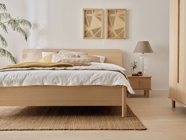 duże łóżko w sypialni, tapicerowany zagłówek, szafa, stoliki nocne, lampa na stoliku, obrazy, dywan, pościel