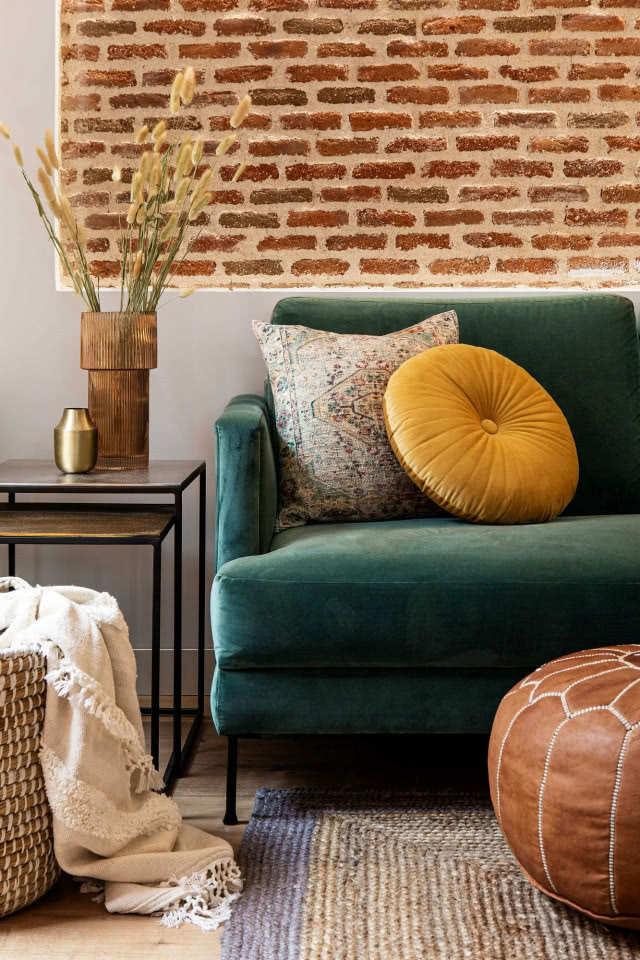 Zielona sofa do salonu na tle ceglanej ściany