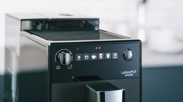 czarny ekspres do kawy, szary blat kuchenny, biała cegłą na ścianie, 