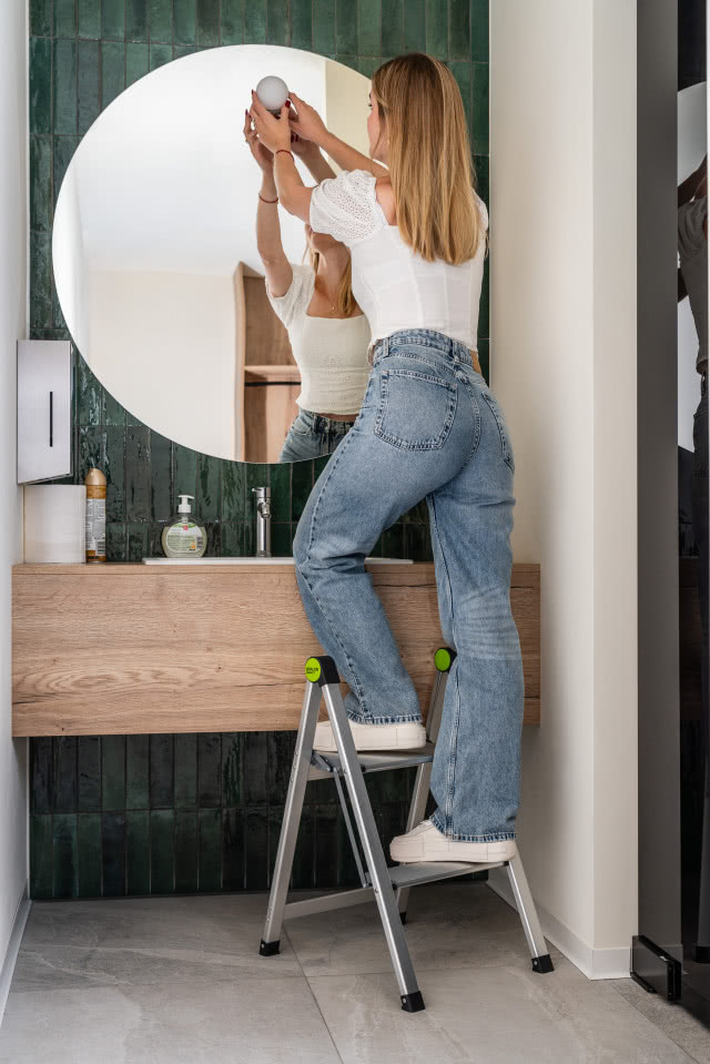 Kobieta stoi na drabinie i wkręca żarówkę