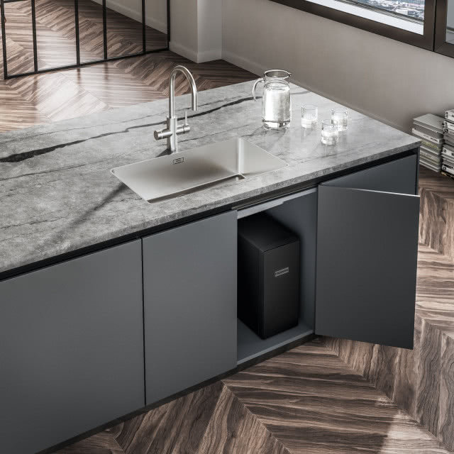 wyspa kuchenna, szary blat, srebrna bateria zlewozmywakowa, zlewozmywak wpuszczony w blat, dzbanek, szklanki z wodą