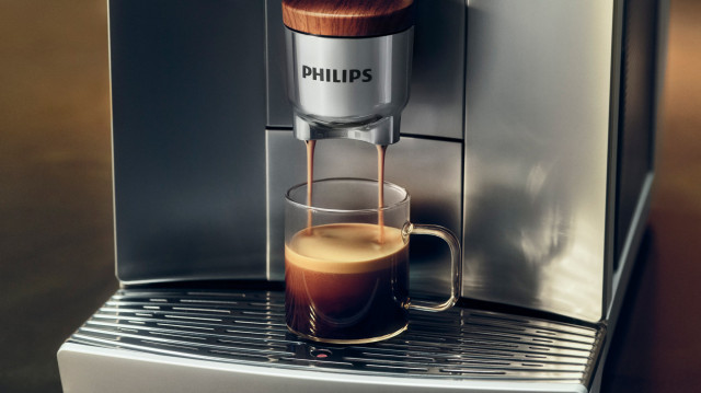 Ekspres Philips LatteGo Pro 8000 przygotowuje aromatyczną kawę w szklanej filiżance. Zbliżenie na proces parzenia espresso z kremową pianką.