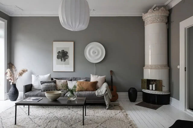 szara ściana z wiszącą ozdobą, lampą i białym kominkiem