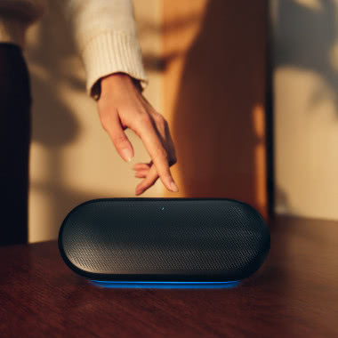 Harman Kardon Luna 2 – bezprzewodowy głośnik Bluetooth z podświetleniem ambientowym na drewnianym stole w domowym wnętrzu