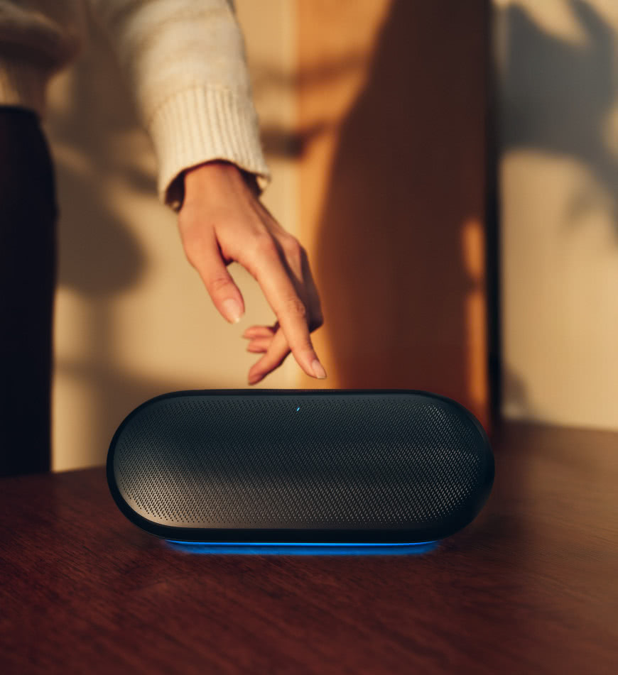 Harman Kardon Luna 2 – bezprzewodowy głośnik Bluetooth z podświetleniem ambientowym na drewnianym stole w domowym wnętrzu