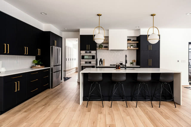 czarne matowe fronty kuchenne, złote uchwyty, płyta gazowa, wyspa kuchenna, okap, zmywarka, czarna bateria zlewozmywakowa, stół, krzesło, dywan, drewniana podłoga
