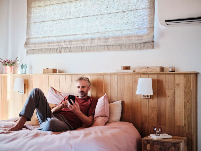 sypialnia, mężczyzna leży na łóżki i steruje telefonem, kinkiety, roleta, klimatyzacja, stolik nocny