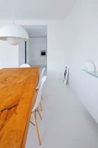 Drewniany stół ociepla białe minimalistyczne wnętrze