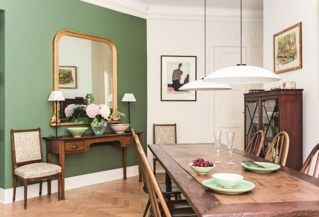 Monotonną biel ścian przełamano, pokrywając część z nich odważnymi kolorami (farby Farrow & Ball). Nad konsolą zawieszono wiktoriańskie lustro w złoconej, drewnianej ramie. Obok stoją XVIII-wieczne krzesła, które zostały obite
współczesną tkaniną firmy GP & J Baker.