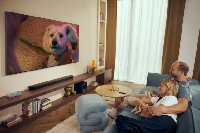 Para odpoczywająca na sofie w nowoczesnym salonie podczas oglądania telewizora Samsung z systemem nagłośnienia.