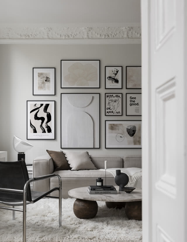 salon w szarościach, na ścianie kilka obrazów powieszonych obok siebie 